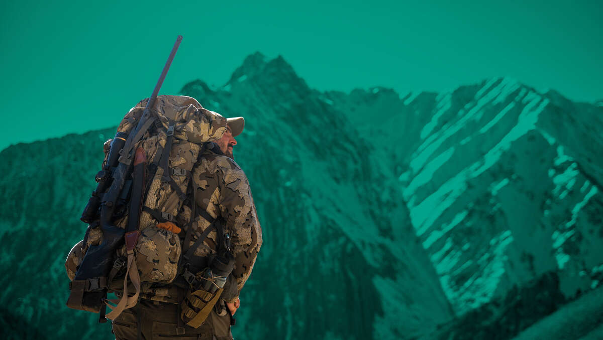 Man in camo with rifle in a sling over the shoulder as climbing
