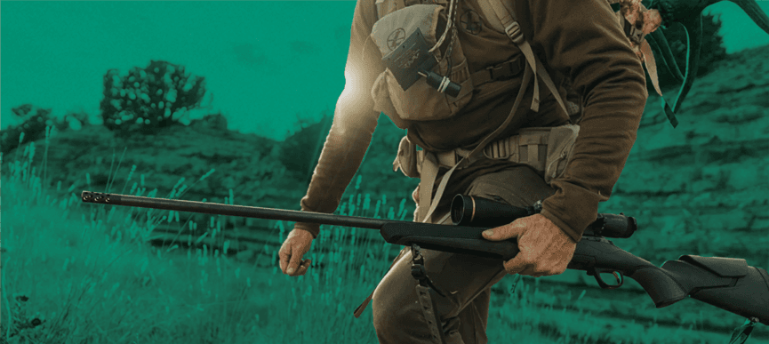 man walking up hill holding rifle