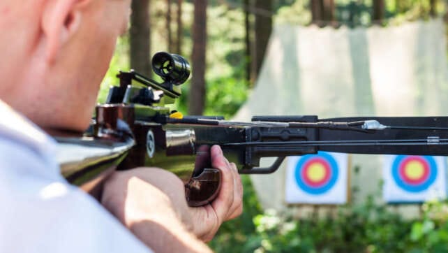 man aiming crossbow at targets
